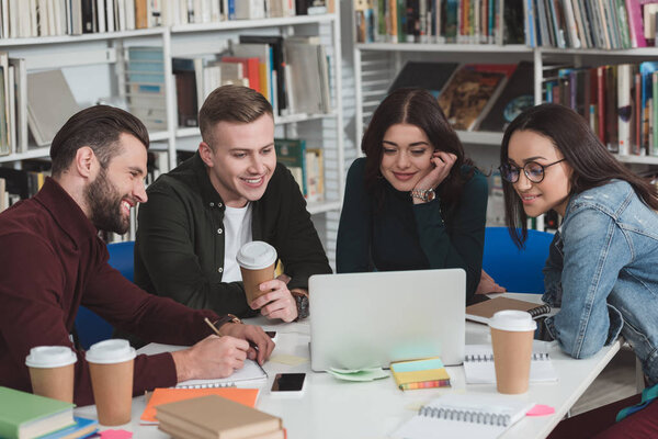 happy multicultural students looking at laptop in library