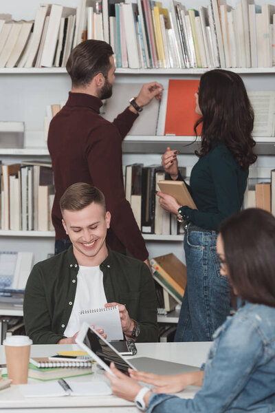 smiling students studying in library with tablet and notebook