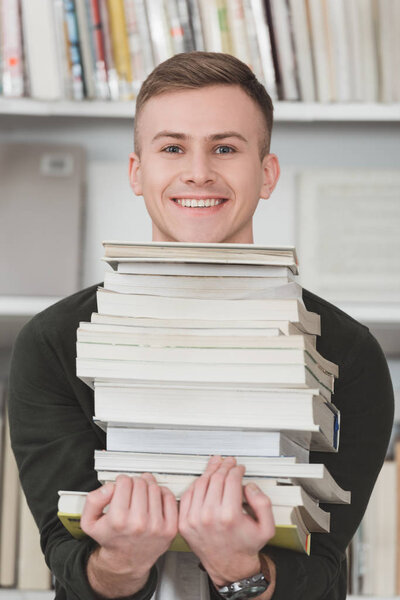 smiling student holding stack of books and looking at camera