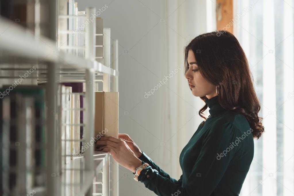 beautiful girl taking book from shelf
