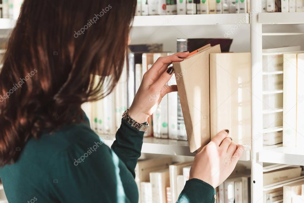 side view of student taking book from shelves in library