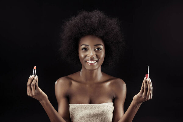 красивая африканская американка, держащая помады изолированные на черном
