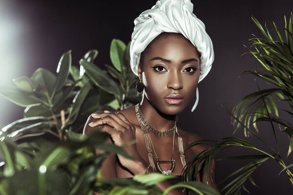 fashionable african american woman in white wire head wrap behind leaves