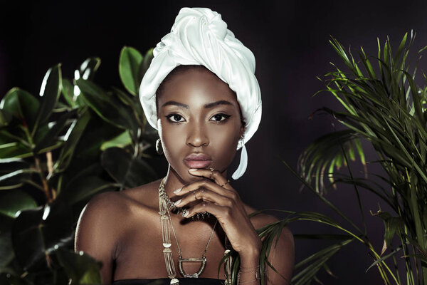 young african american woman in white wire head wrap behind leaves looking at camera