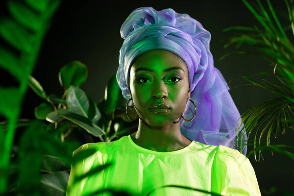 young african american woman in traditional wire head wrap under green light looking at camera