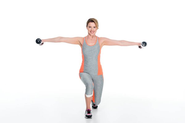 Улыбающаяся женщина в спортивной одежде, упражняющаяся с гантелями, изолированными на белом
