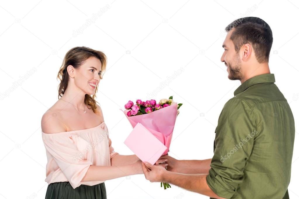 side view of man presenting bouquet of flowers and postcard to wife isolated on white