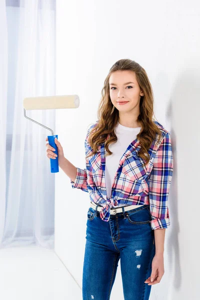 smiling girl holding paint roll brush and looking at camera