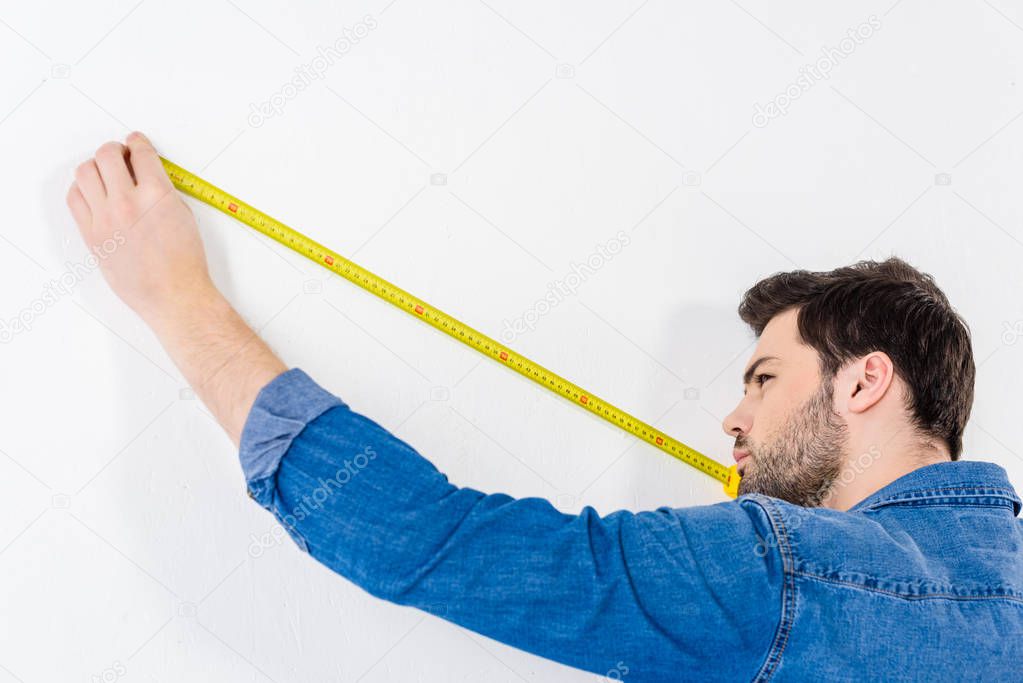 man measuring wall with tape measure on white