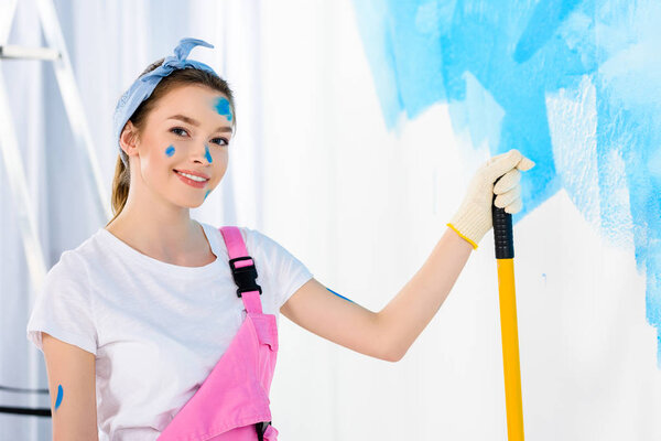 smiling girl holding paint roller brush and looking at camera