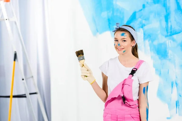 smiling girl holding paint brush and looking at camera