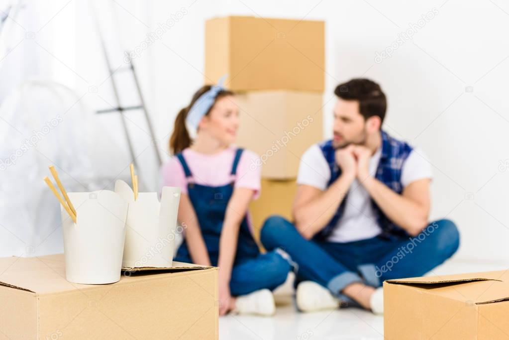 boyfriend and girlfriend sitting on floor with noodles on foreground
