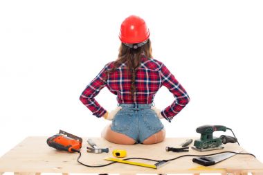 back view of sexy girl in hardhat sitting on wooden table with tools, isolated on white