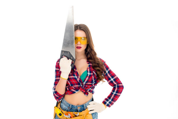 beautiful girl in goggles with tool belt holding saw, isolated on white
