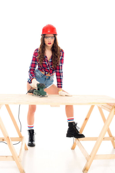 sexy girl in safety helmet working with grind tool at wooden table, isolated on white
