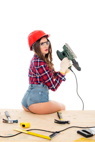 sexy girl posing with grind tool on wooden table with tools, isolated on white