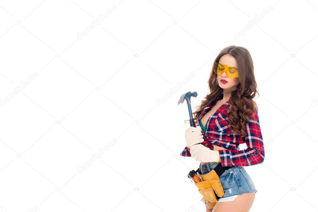 sexy woman in goggles and gloves with tool belt holding hammer, isolated on white