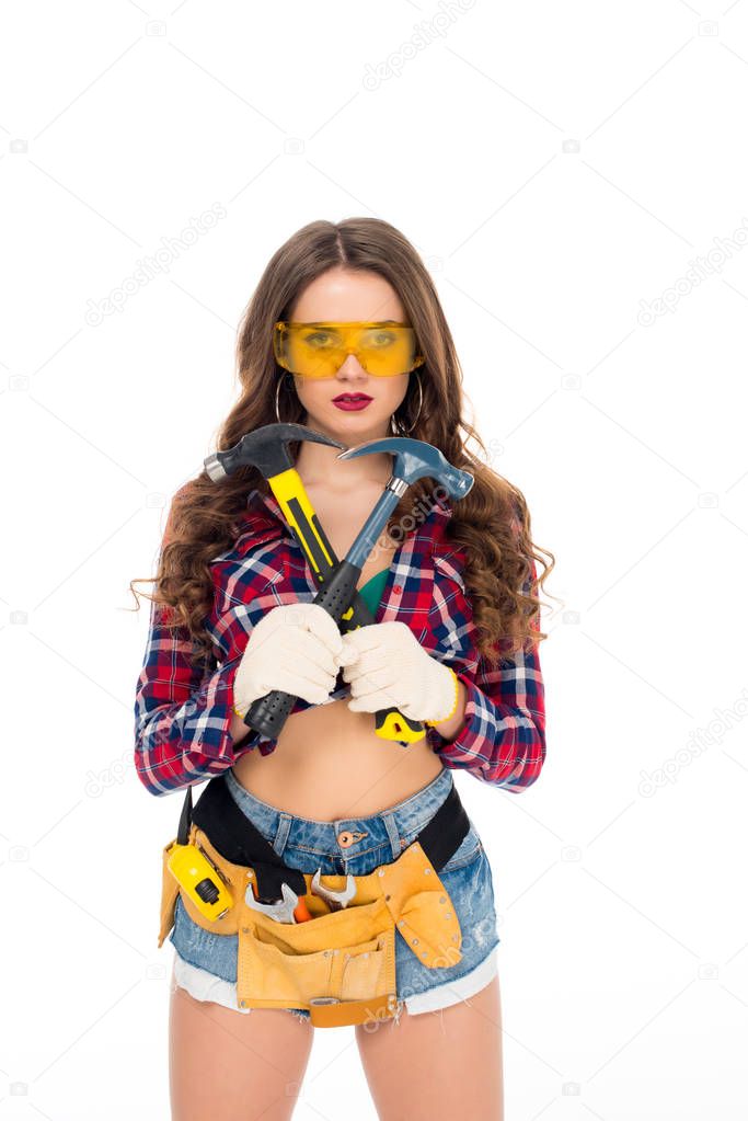 beautiful girl in goggles and gloves with tool belt holding hammers, isolated on white