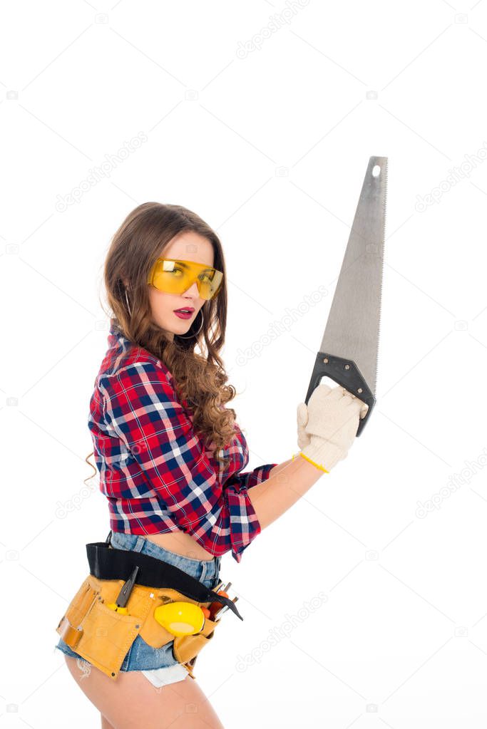 beautiful sexy girl in goggles with tool belt holding saw, isolated on white