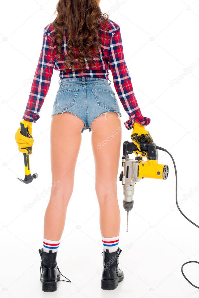 cropped view of sexy girl in gloves holding hammer and electric drill, isolated on white