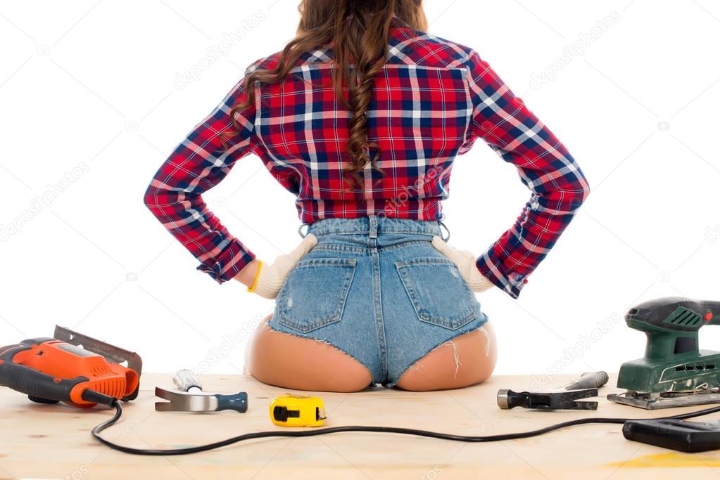 back view of sexy girl sitting on wooden table with tools, isolated on white