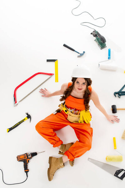 overhead view of girl in overalls sitting on floor with different equipment and tools, isolated on white