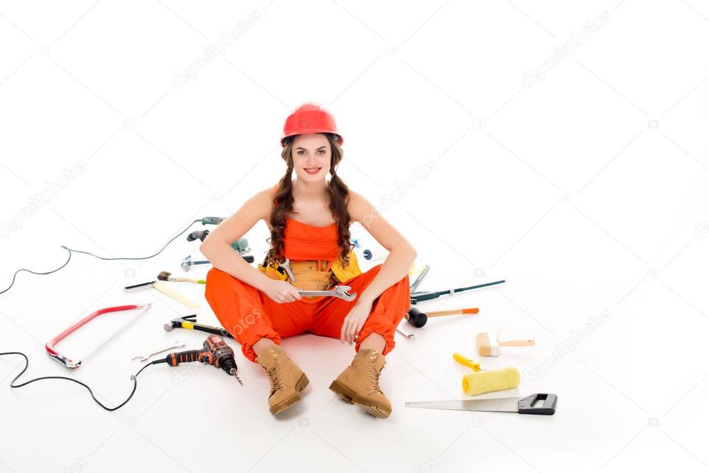 girl in overalls sitting on floor with different equipment and tools, isolated on white