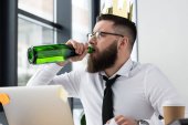 businessman with paper crown on head drinking champagne at workplace in office