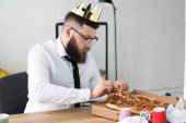 businessman in paper crown sitting at workplace with pizza