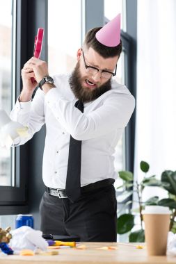 businessman with party cone on head crashing toy guitar in office clipart