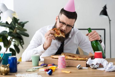İşyerinde pizza yemek başında parti koni ile işadamı