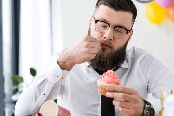 portrait of businessman holding birthday cupcake in hands in office