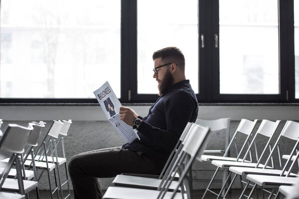 side view of focused businessman reading newspaper while sitting in meeting room