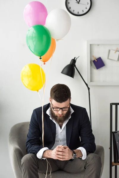 肘掛け椅子に座っているカラフルな風船を持ったビジネスマン — ストック写真