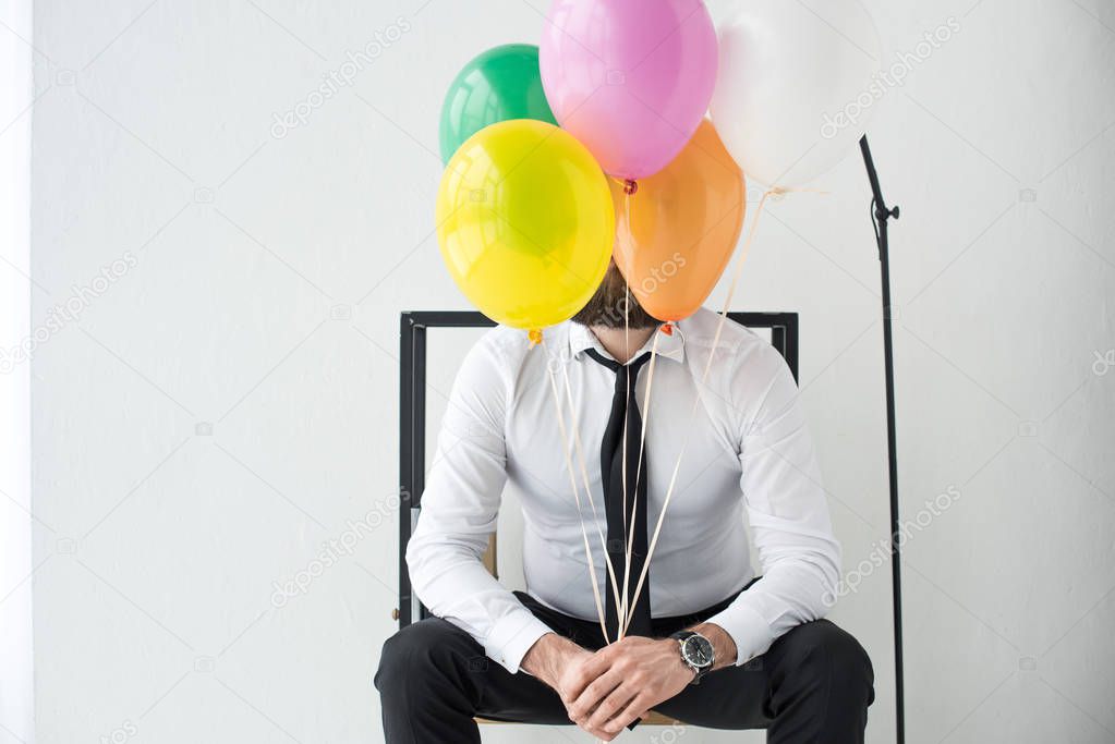 obscured view of businessman with colorful balloons sitting on chair