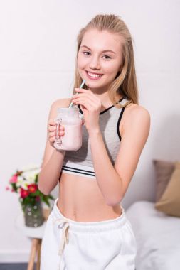smiling young woman with milkshake in mason jar with straw looking at camera clipart