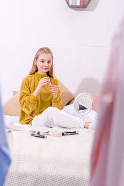 young woman doing makeup while sitting on bed at home clipart