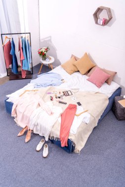 high angle view of interior of modern bedroom with hanger full of various female clothing and makeup supplies on bed clipart