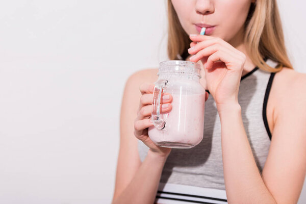 cropped shot of young woman drinking milkshake from mason jar with straw