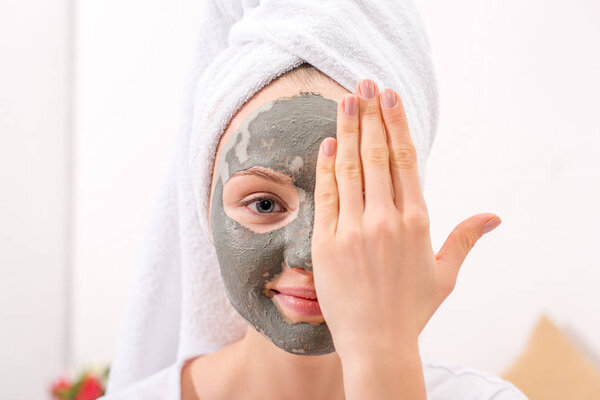 young woman with cosmetic clay mask covering half of face