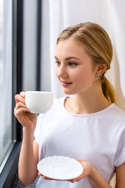 Glad Ung Kvinna Dricker Kaffe Och Tittar Genom Fönstret — Stockfoto