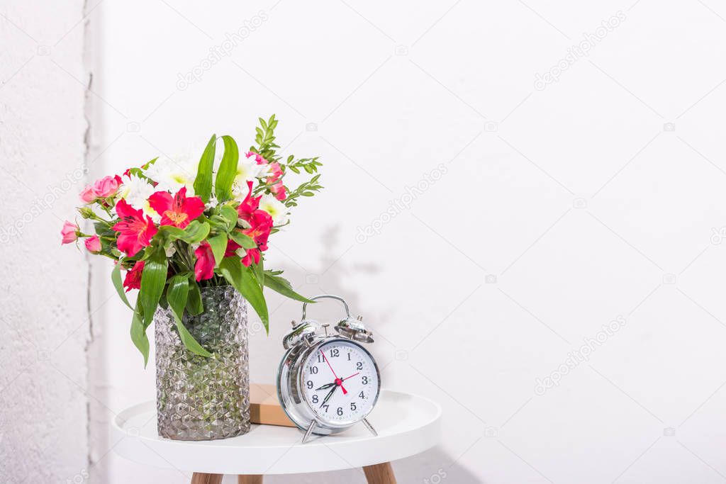 vintage alarm clock on table with flowers in vase