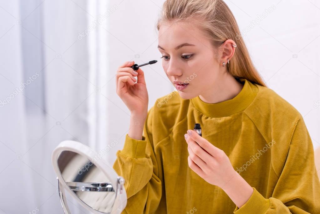 young woman applying mascara and looking at mirror