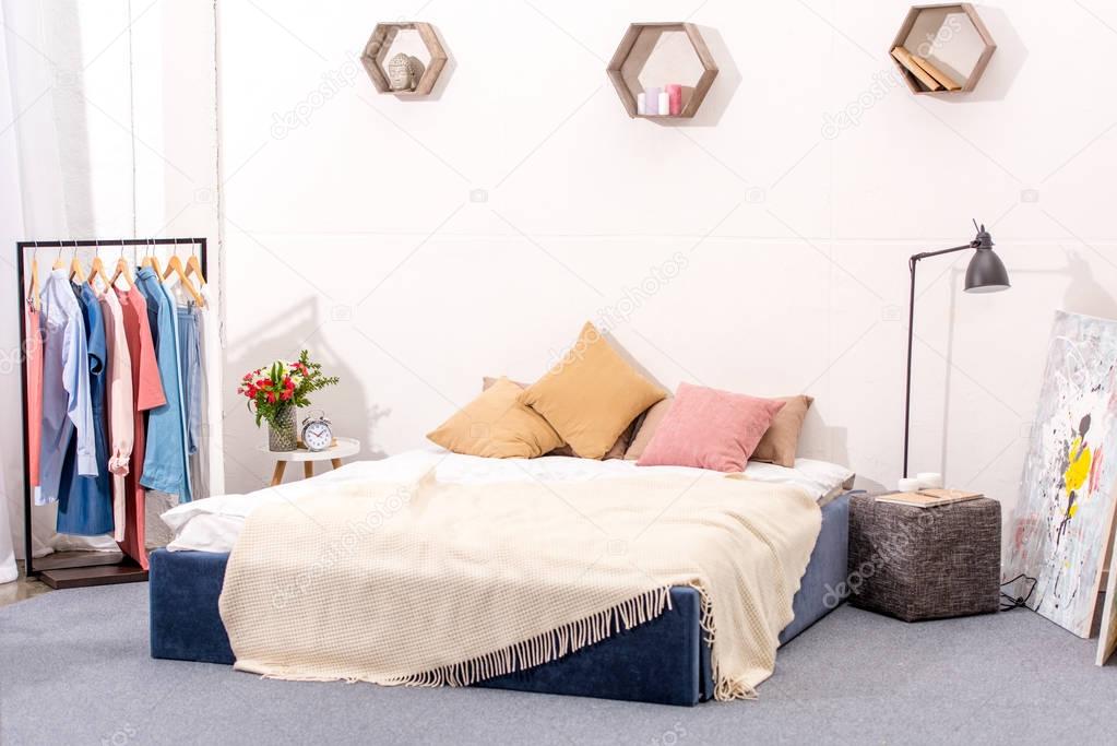 interior of bedroom with stylish decor and hanger full of various female clothing
