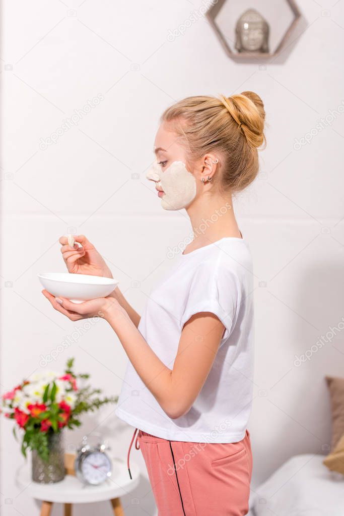 side view of young woman applying clay mask on face at home