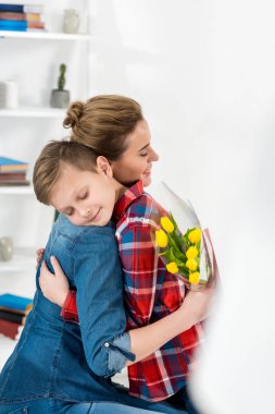 Anne ve oğlu ona çiçek verdikten sonra Anneler gününde kucaklayan