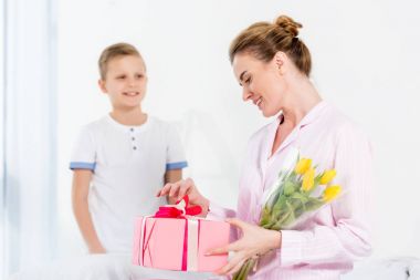 son presenting gift and flowers for his beautiful happy mother on mothers day morning clipart
