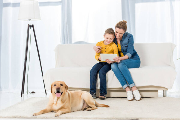 mother and son using tablet together with adorable dog lying on floor on foreground