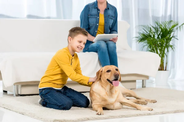 Niño Feliz Acariciando Perro Suelo Mientras Que Madre Usando Tableta — Foto de Stock