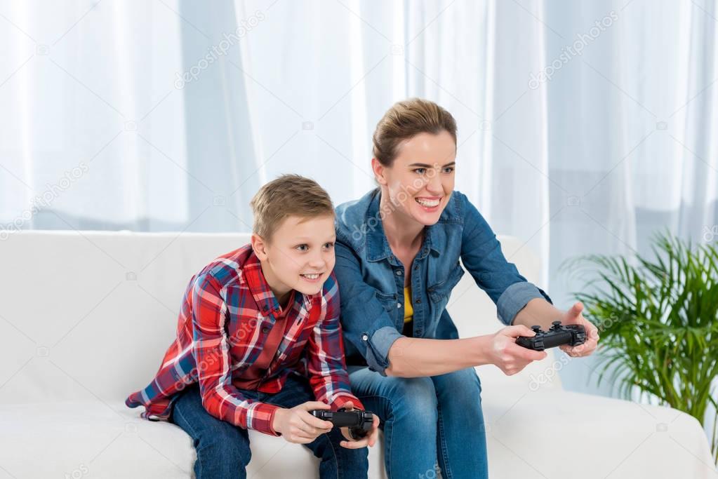 excited mother and son playing video games with gamepads together on couch